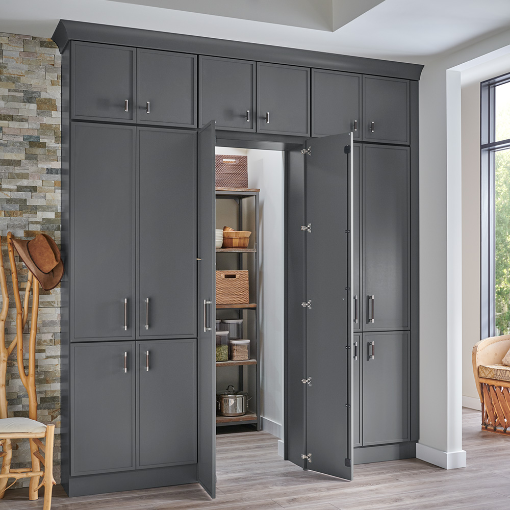 Modern pantry with dark gray cabinetry, open doors revealing rustic shelving stocked with baskets, bowls, and clear containers of spices and dried goods.